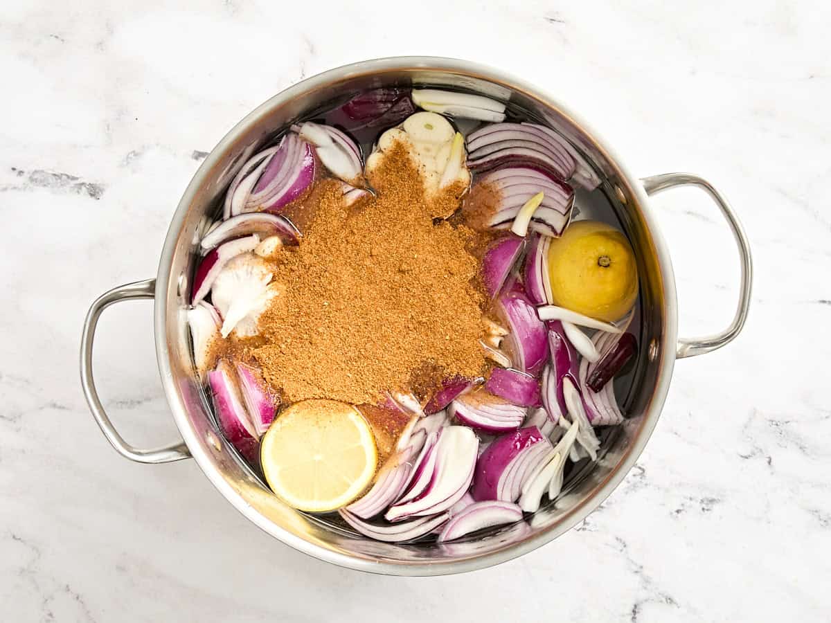 A pot of water with red onion, old bay seasoning, lemon, and garlic.