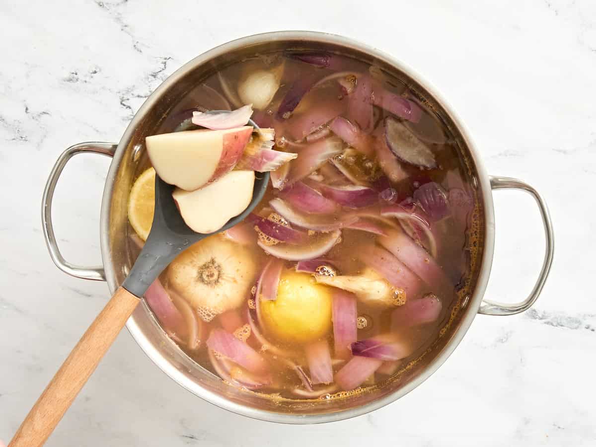 Potatoes, red onions, garlic and lemon wedges in a simmering pot of water.