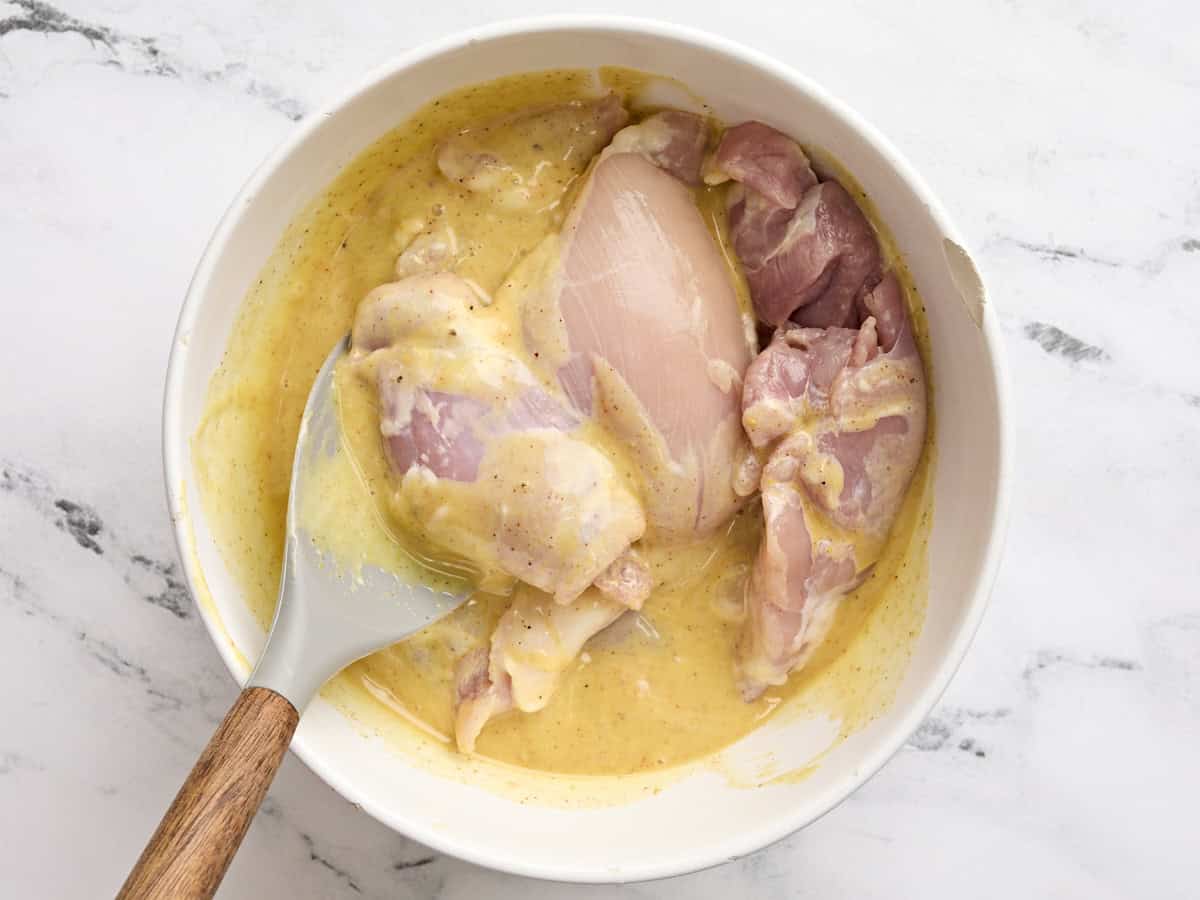 Boneless and skinless chicken thighs added to a bowl with honey mustard sauce.