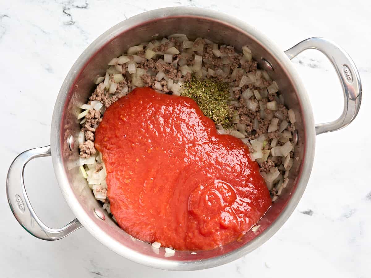 Crushed tomatoes added to browned ground beef in a skillet with seasonings.