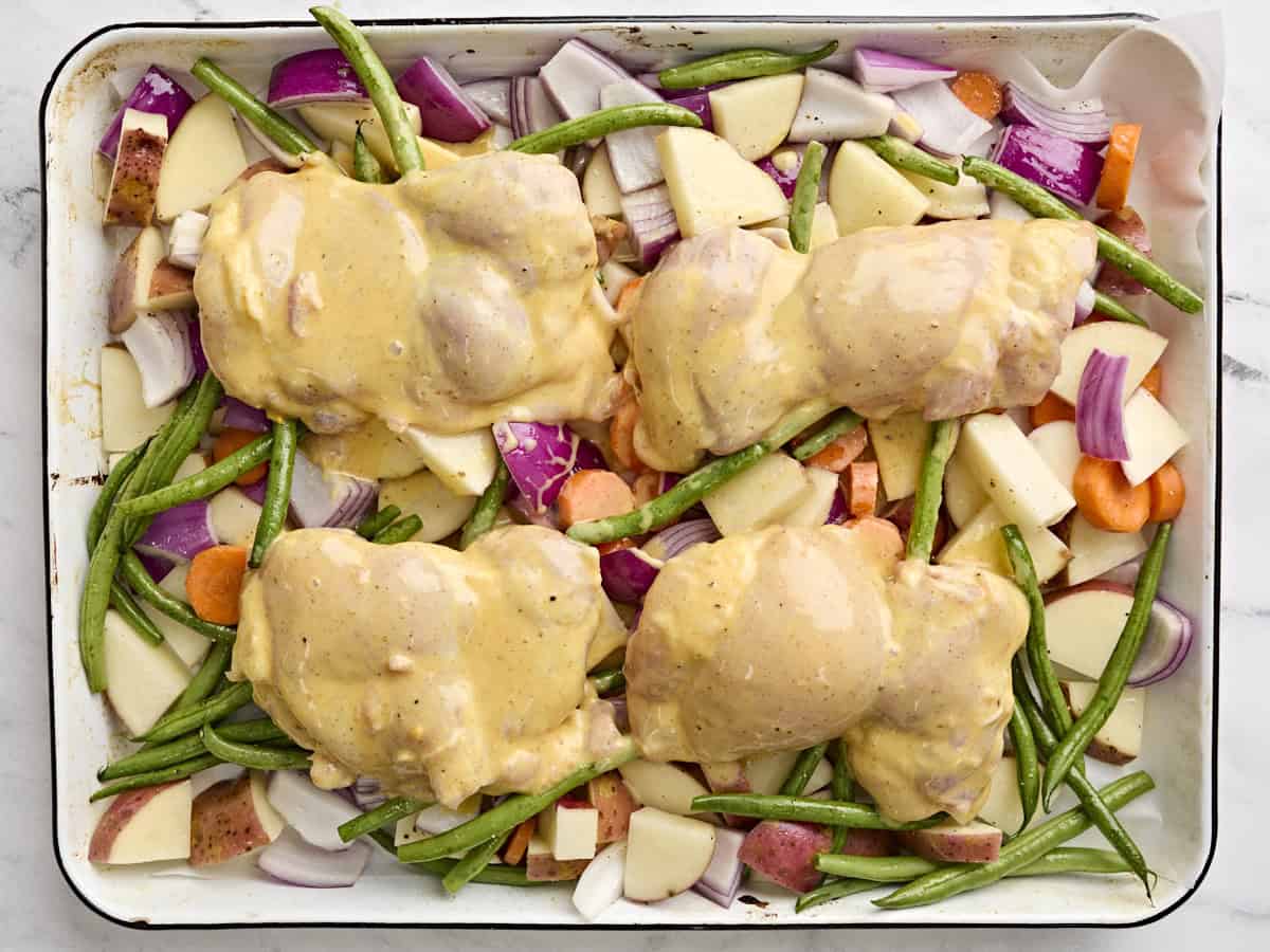Honey mustard chicken added to a sheet pan with vegetables.