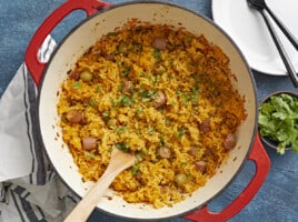 Overhead shot of wooden spoon in a red Dutch oven full of Arroz Con Salchichas.