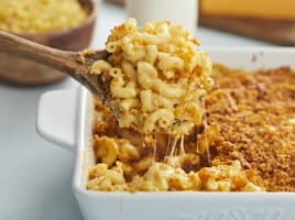 Side view of baked mac and cheese being lifted out of the casserole dish with a wooden spoon.