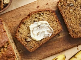 Overhead view of a slice of banana bread with butter spread on it.
