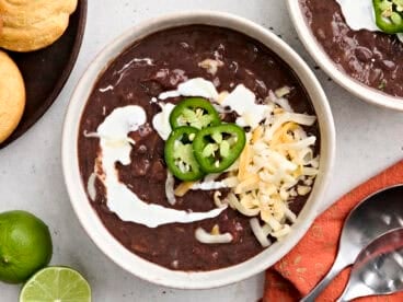 Overhead view of a bowl of black bean soup, topped with jalapeno slices, shredded cheese, and sour cream.