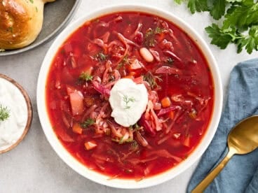 Overhead view of a bowl of borscht topped with sour cream and fresh herbs.