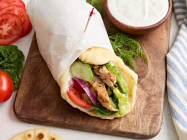 Side view of a chicken shawarma wrap, wrapped in parchment paper.