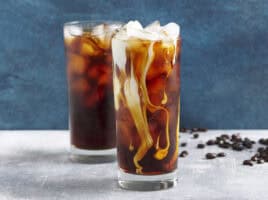 Side view of two glassed of cold brew coffee with ice, one with cream added.