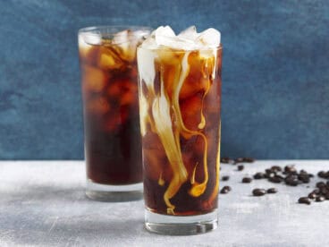 Side view of two glassed of cold brew coffee with ice, one with cream added.