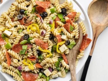 Close up of a serving bowl of pizza pasta salad, a wooden spoon in the side