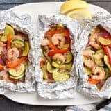 Overhead view of grilled shrimp and vegetable foil packets on a serving platter.